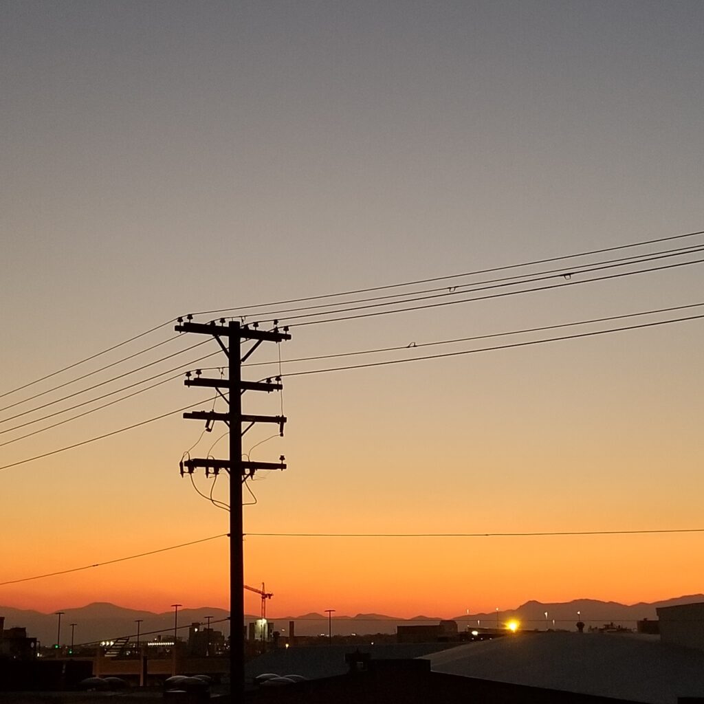 Photo of stark contrast of a power line and wires at sunset with the mountains in the background.